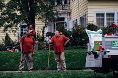 Three men in red shorts with yard maintenance tools standing in a front yard